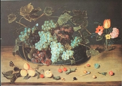Glass of flowers and plate with grapes